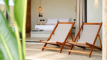 A bedroom with a bed, two wooden chairs, a bedside table, a wall-mounted lamp, and a view of the outdoors.