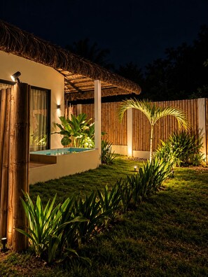 A modern house with a thatched roof, a swimming pool, and a bamboo fence.