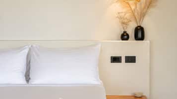 A bedroom with a bed, pillows, a bedside table, a lamp, and a vase with dried plants.