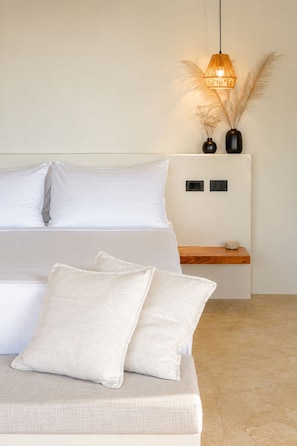 A bedroom with a bed, pillows, a bedside table, a lamp, and a vase with dried plants.