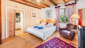 A bedroom with a wooden ceiling, a bed with white linens, a brown leather chair, and a window with curtains.