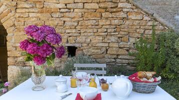 Una mesa servida con alimentos para el desayuno, un jarrón de flores y un fondo de pared de piedra.
