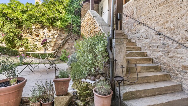 A stone staircase leading to a wooden door, surrounded by potted plants and a metal table with chairs.