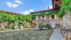 A courtyard with a stone wall, a wooden pergola, and a small archway.