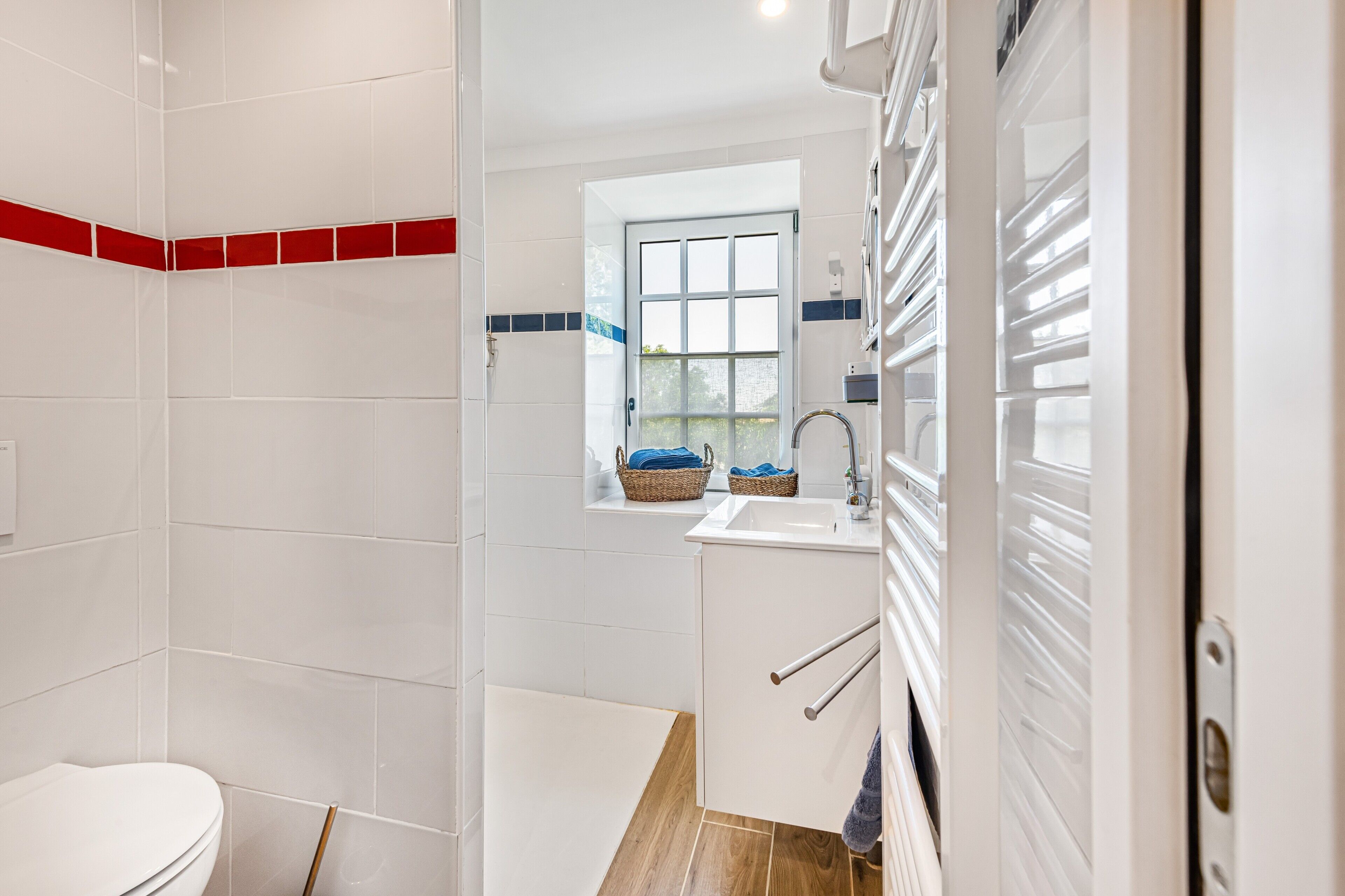 A bathroom with a toilet, a shower area, and a sink with a window above it.