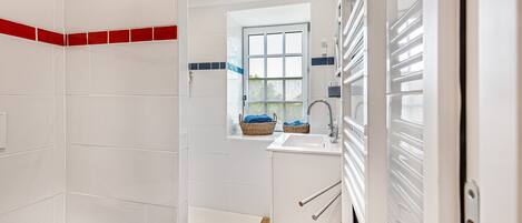 A bathroom with a toilet, a shower area, and a sink with a window above it.