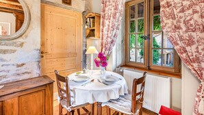 A room with a round table set for dining, wooden chairs, a mirror, a wooden door, and a window with curtains.