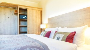 Hotellihuone, jossa on suuri sänky, puinen pääty ja vaatekaappi hyllyineen.