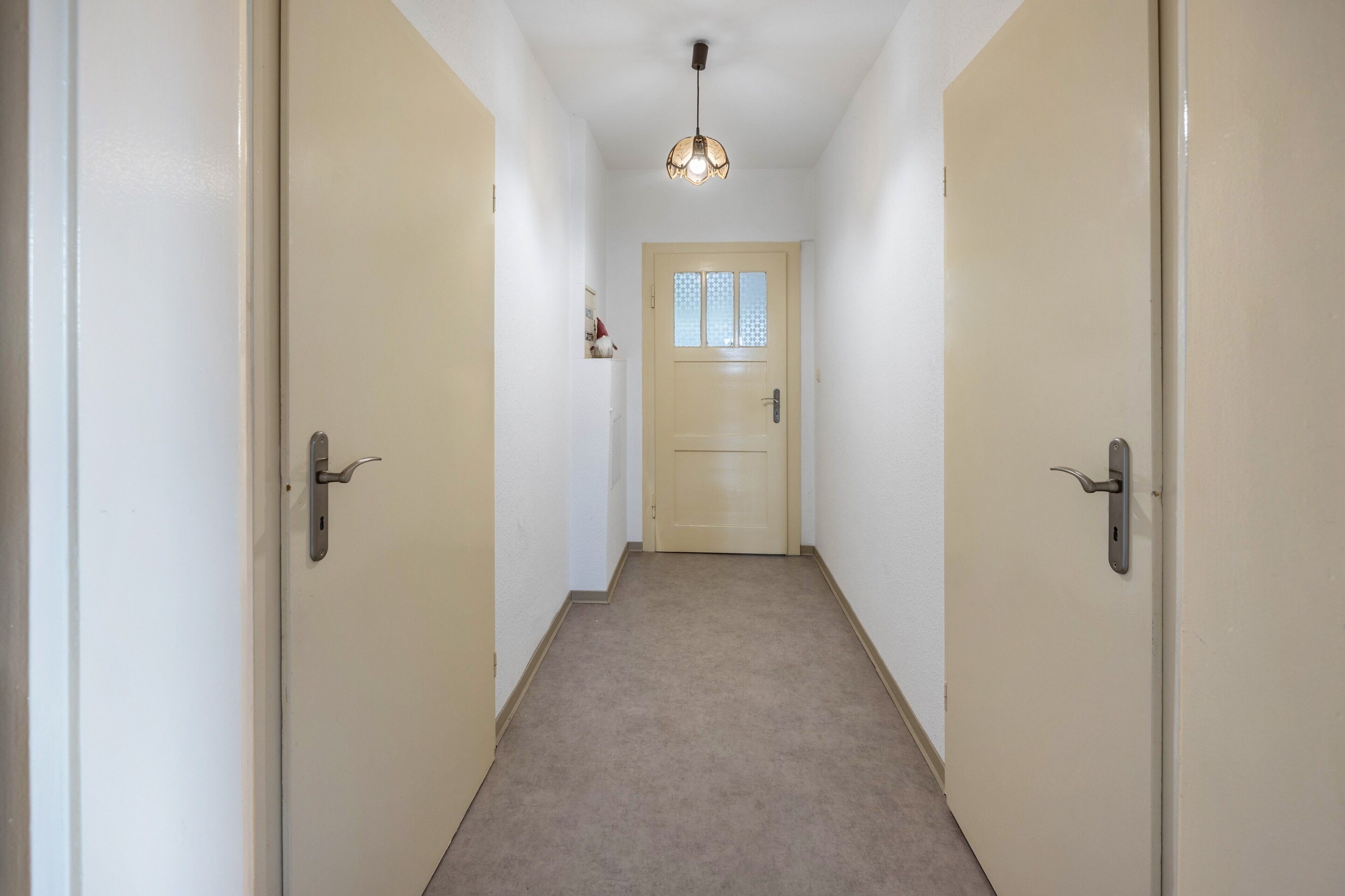 A hallway with carpeted floors, beige walls, and two doors on either side.