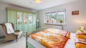 Un dormitorio con cama, una silla, un armario y una ventana con vistas.