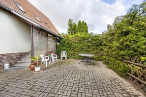 A paved patio with a table and chairs, a potted plant, and a brick wall.