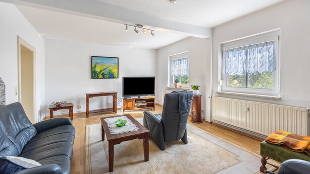 Una sala de estar moderna con un sofá, una mesa de centro, un televisor y un ventanal con cortinas.