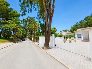 A street lined with palm trees and a white building with a tiled patio.