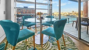 Een moderne kamer met een groot raam, een ronde tafel met stoelen en uitzicht op een jachthaven.