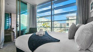 Een moderne hotelkamer met een groot bed, uitzicht op de stad en een balkon met een rieten stoel.