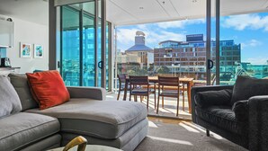 Een moderne woonkamer met een grote glazen deur die uitkomt op een terras, een bank, een salontafel en een eethoek met stoelen.