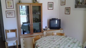A room with a dining table, chairs, a television, a cabinet, and framed pictures on the wall. - Seaside House with Private Entrance, Steps from Beach and Station (Termini)