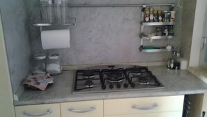 A kitchen with a gas stove, a shelf with bottles, and a paper towel holder. - Seaside House with Private Entrance, Steps from Beach and Station (Termini)