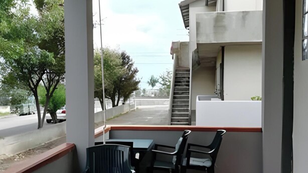 A balcony with a table and chairs, a view of the street and trees, and a building with a staircase. - Seaside House with Private Entrance, Steps from Beach and Station (Termini)