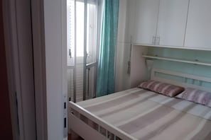 A bedroom with a bed, a window with curtains, and white cabinets.