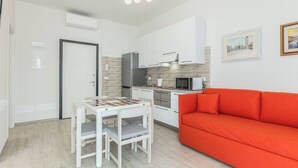 Un espace de vie compact comprenant un coin cuisine, une table à manger avec des chaises et un canapé rouge.