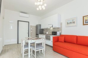 A compact living space with a kitchenette, a dining table with chairs, and a red sofa. - Serenity (Bologna)