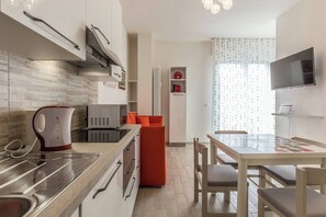 A modern kitchen with white cabinets, a microwave, a kettle, and a dining area with a table and chairs. - Serenity (Bologna)