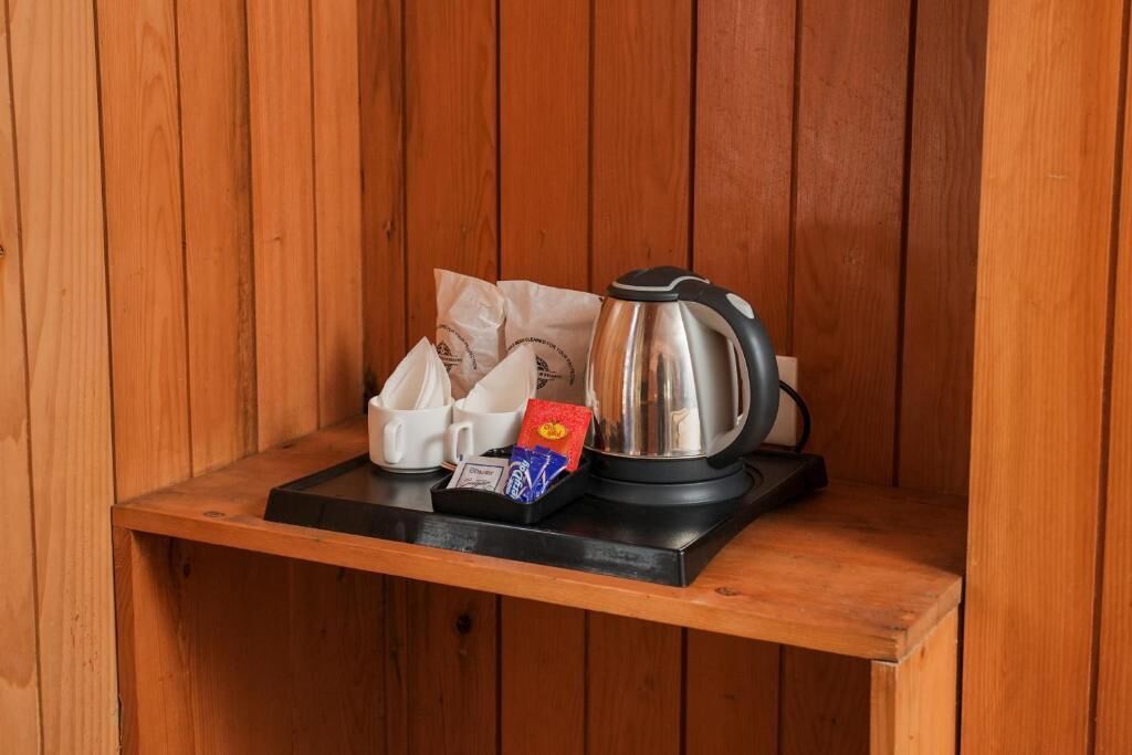A wooden shelf with a kettle, a coffee pod, and a small packet.