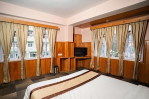 A hotel room with a large bed, wooden paneling, a TV, and windows with curtains. - Verdant The Vintage (Lachung)