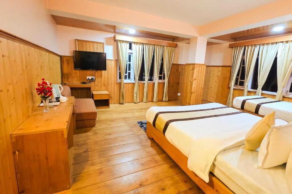A wooden-paneled room with two beds, a flat-screen TV, a wooden desk, and a window with curtains.