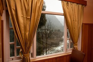 Quarto com janela, cortinas, uma cadeira e vista para uma paisagem montanhosa.