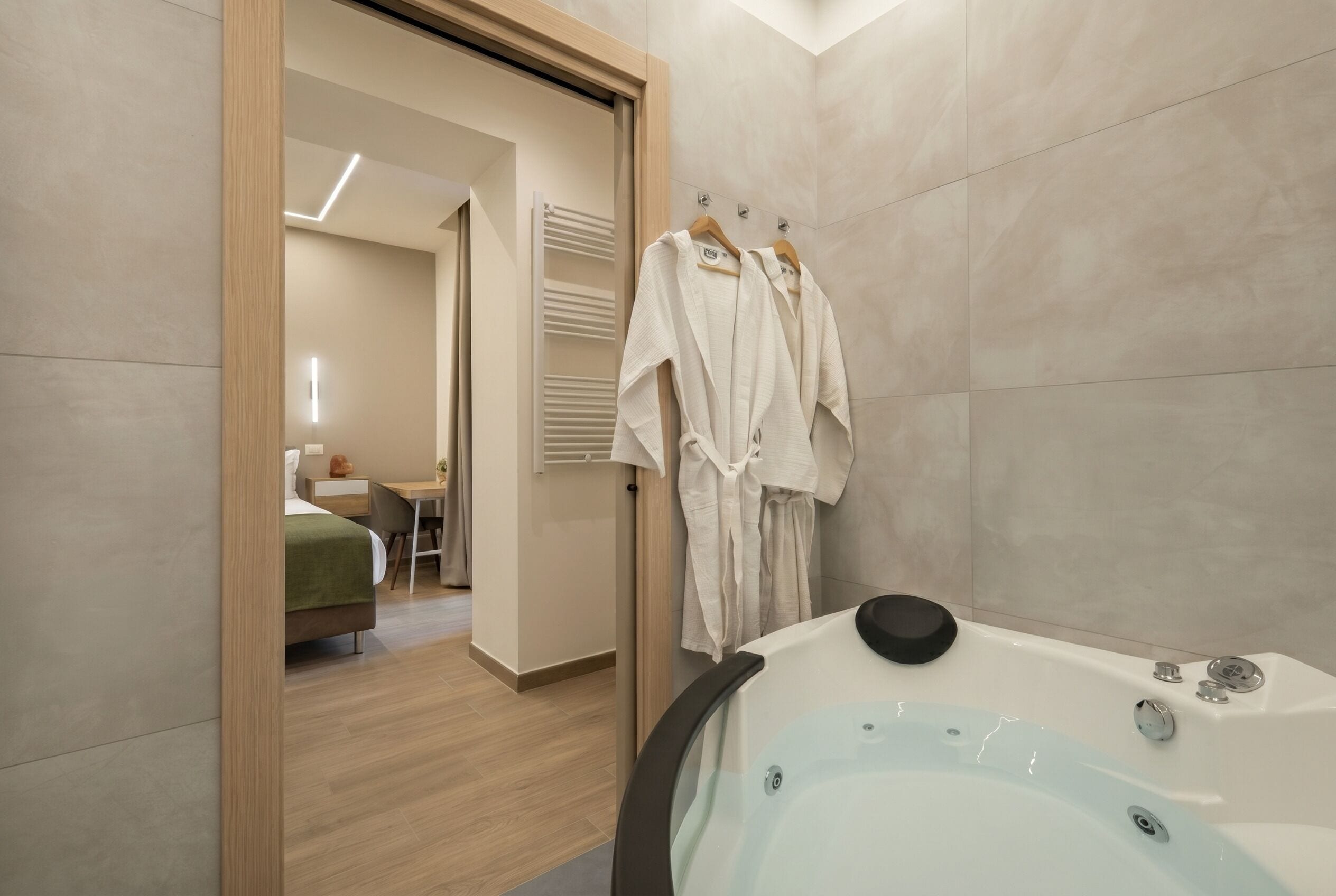 Un bagno moderno con una vasca, una porta in legno e uno scorcio di una camera da letto con un letto e una scrivania.