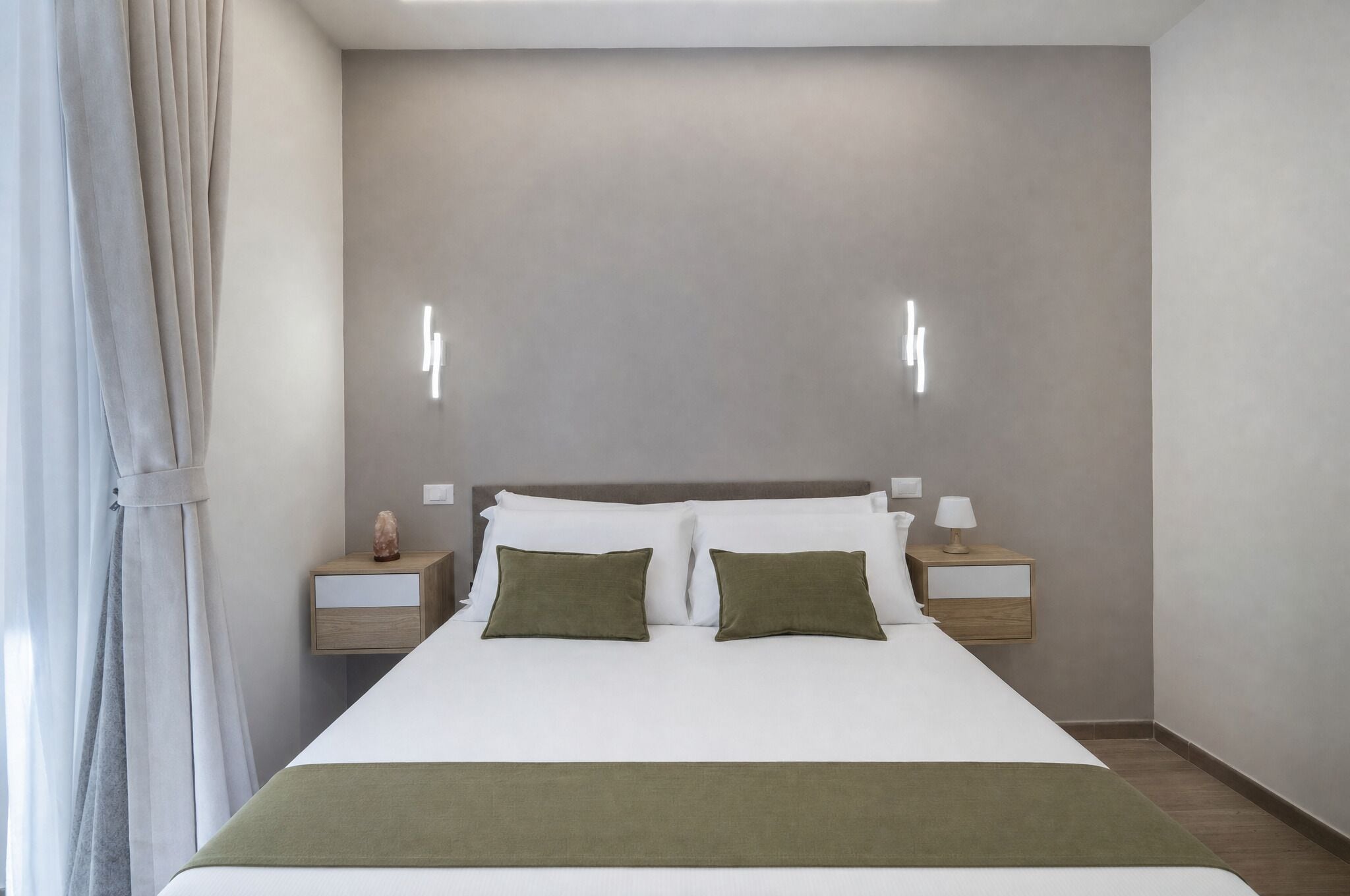 A modern hotel room with a large bed, two bedside tables, and a neutral color scheme.