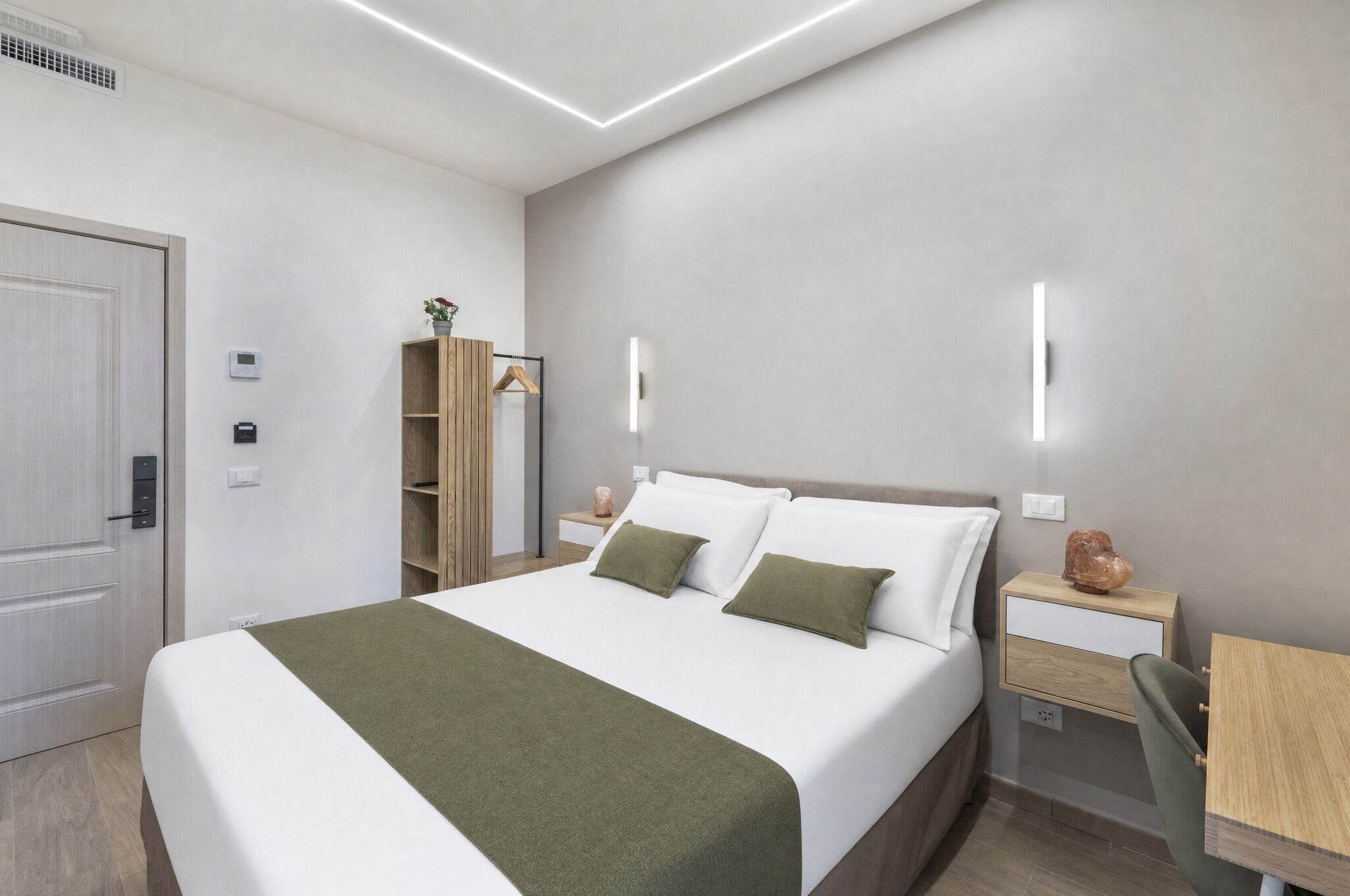 A modern hotel room with a bed, bedside tables, a wardrobe, and a desk.