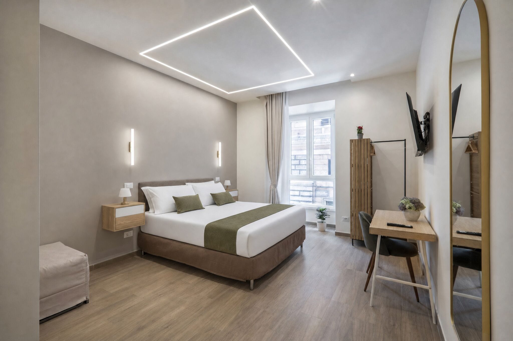 Ett modernt hotellrum med en säng, sängbord, ett skrivbord och en stor spegel.