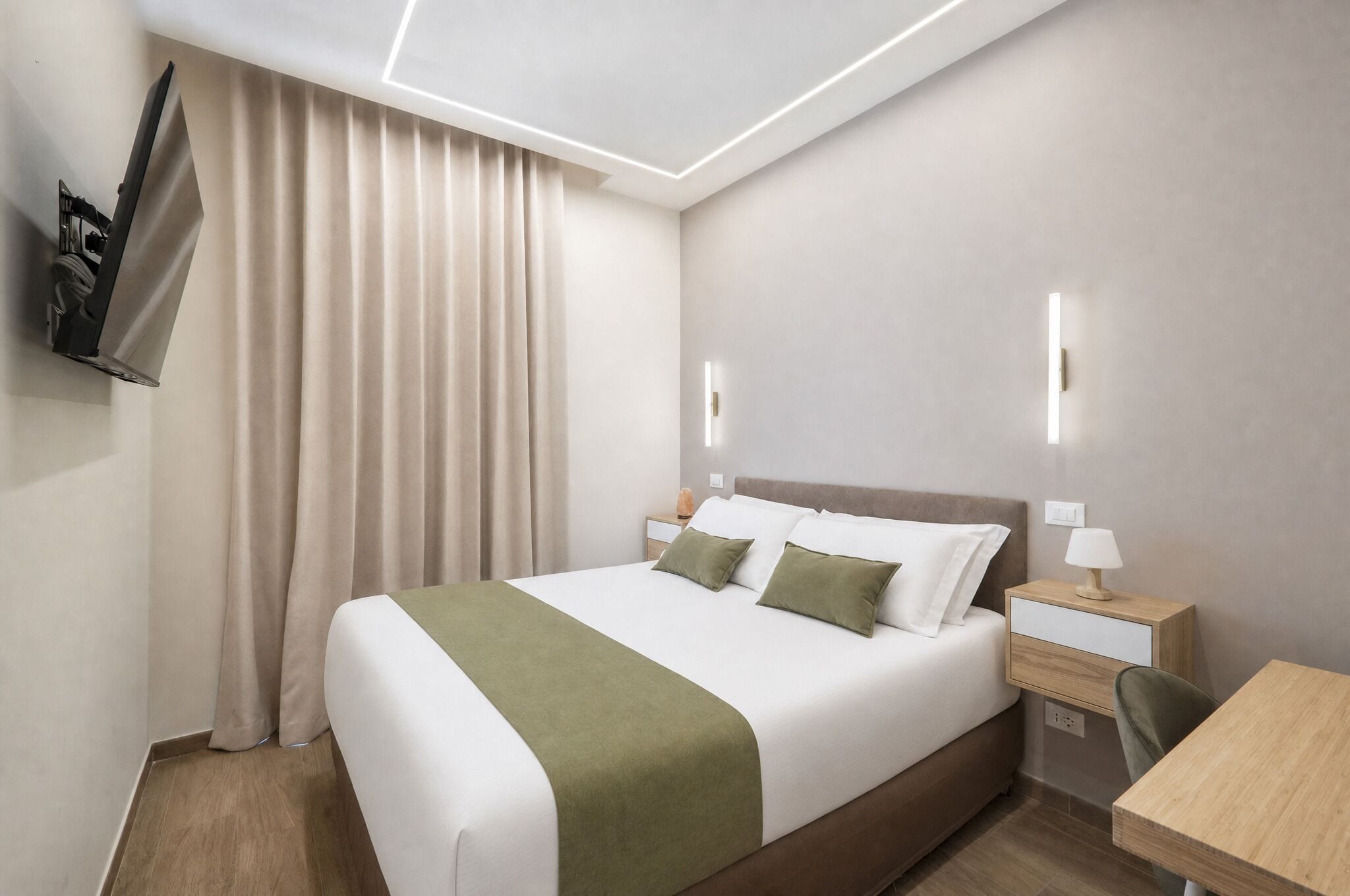 Una habitación de hotel con una cama, mesitas de noche, un escritorio y un televisor montado en la pared.