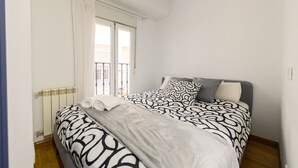 Et soveværelse med seng, radiator, vindue med gardiner og en balkon.