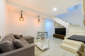 A modern living room with a sofa, coffee table, TV, and staircase. - (PRA100C) 2 bedroom and 2 bathroom apartment in the center of Madrid (Madrid)