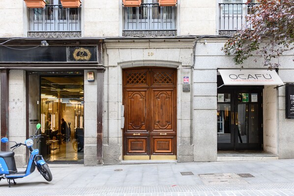 A building with a large wooden double door, a scooter parked in front, and a sign reading 'OCAFU'. - (PRA100C) 2 bedroom and 2 bathroom apartment in the center of Madrid (Madrid)