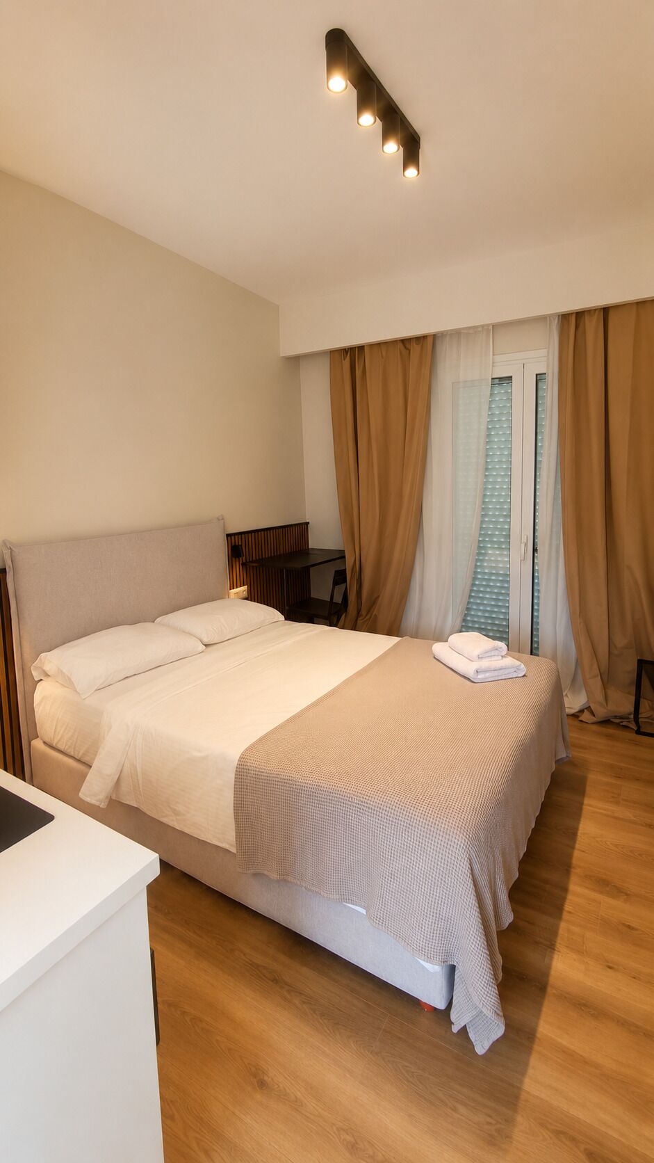Een hotelkamer met een bed, nachtkastje en een raam met gordijnen.