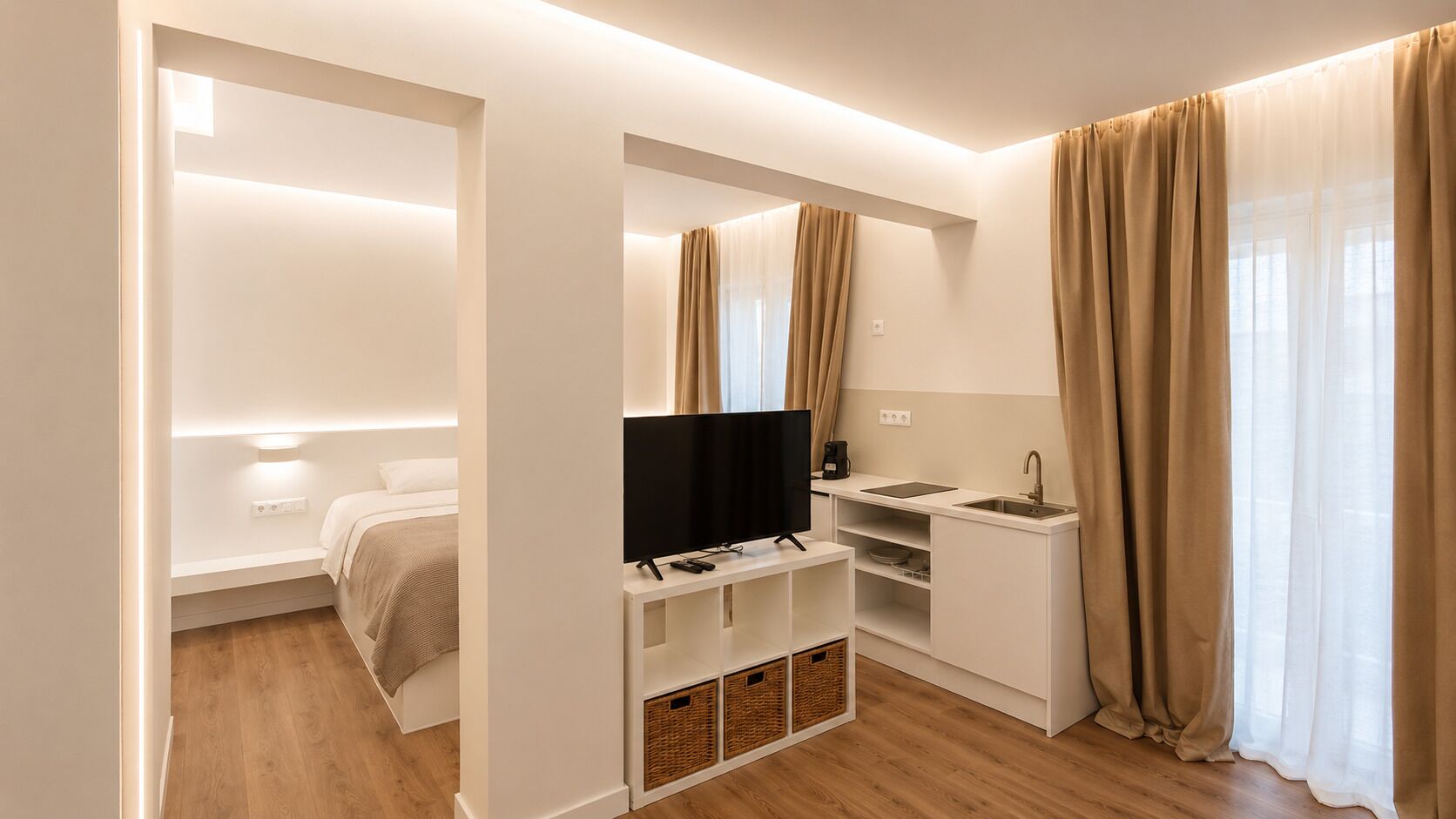 A modern hotel room with a bed, TV, kitchenette, and a bathroom.