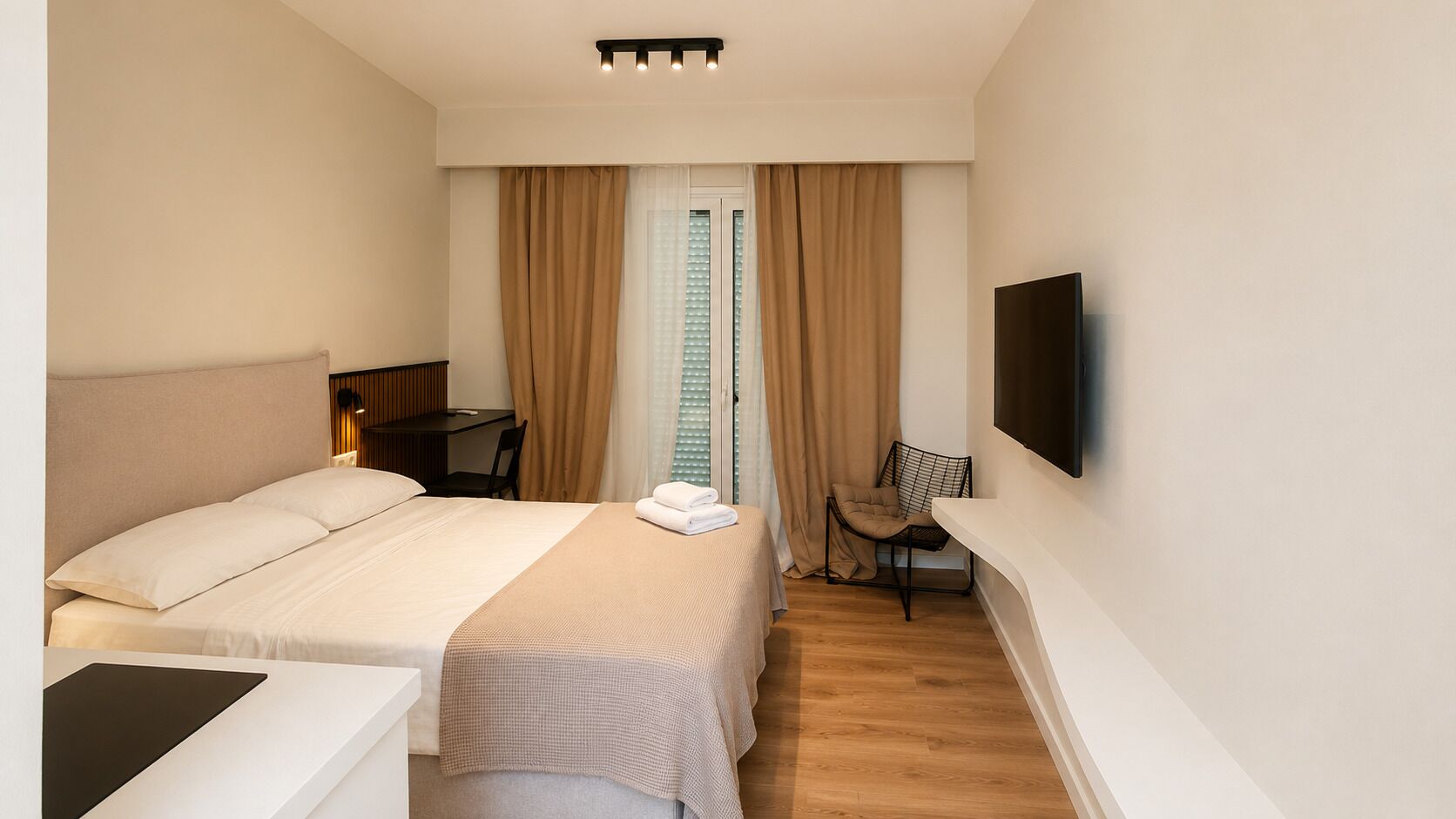 Habitación de hotel con cama, escritorio, silla, televisión y ventana con cortinas.