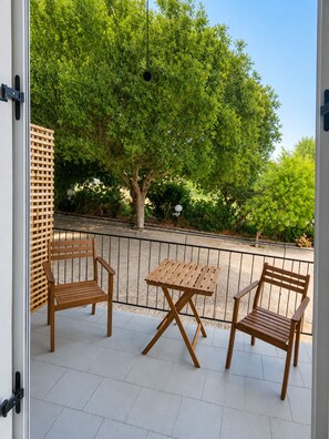 An outdoor patio with two wooden chairs and a table, a wooden lattice fence, and a tree in the background.