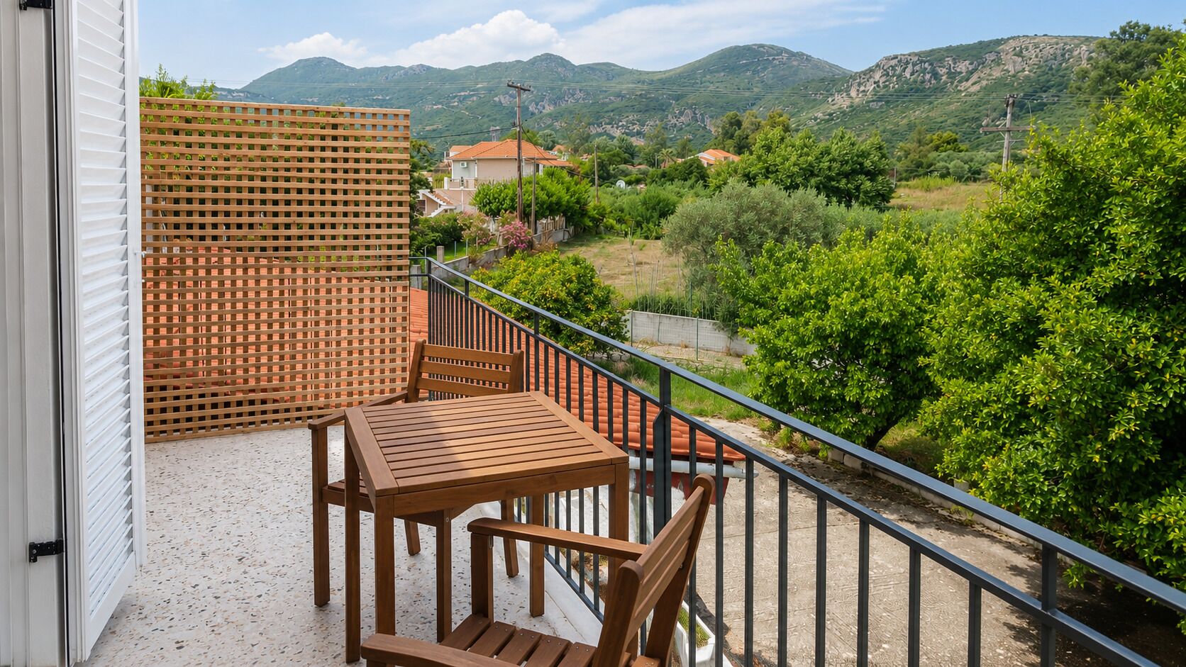 A balcony with a wooden table and chairs, a wooden lattice partition, and a view of a green landscape with hills.