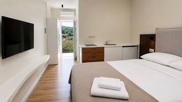 Un dormitorio con televisor, cama con ropa blanca, baño con lavamanos y vistas a zonas verdes.