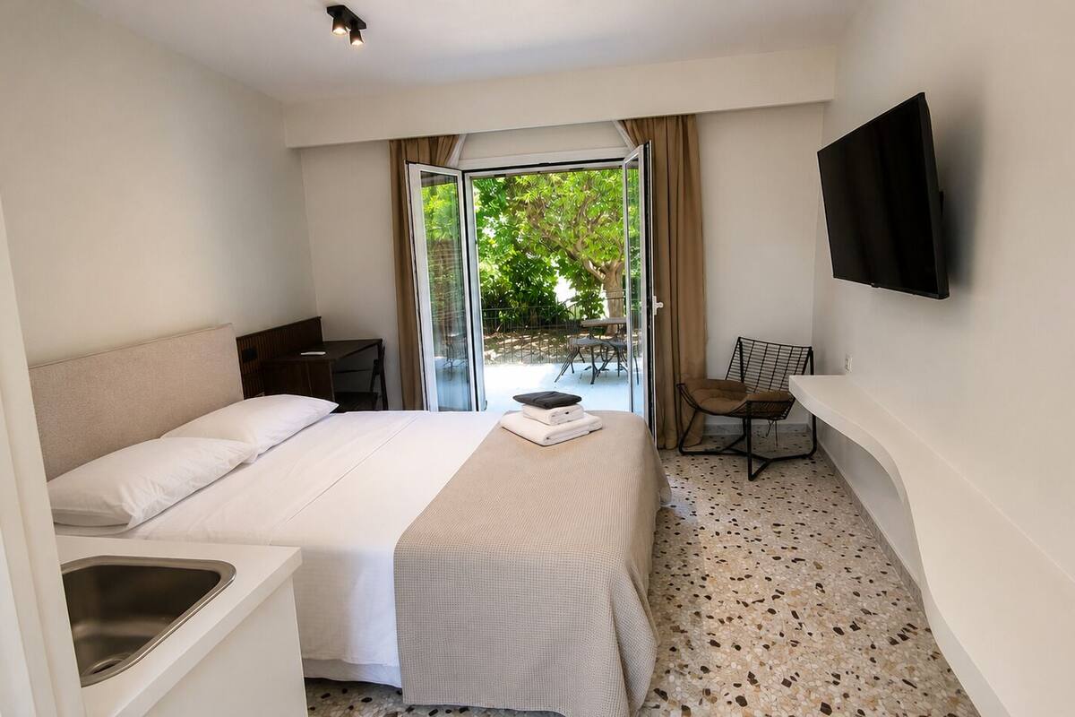 A hotel room with a bed, a desk, a chair, a TV, and a view of the outdoors.