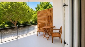 A balcony with a wooden table and chairs, a metal railing, and a view of a tree and a fence. - Elysium Apartments (Kefalonia)