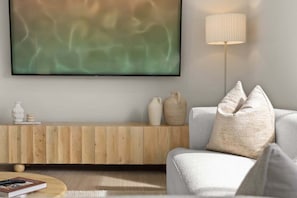 Ein modernes Wohnzimmer mit Flachbildfernseher, einem Holztischelement, einer Couch mit Kissen und einer Stehlampe.