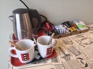 Una taula amb dues tasses blanques amb dissenys vermells i negres, una tetera d'acer inoxidable i un safata amb bolígrafs i llibretes.