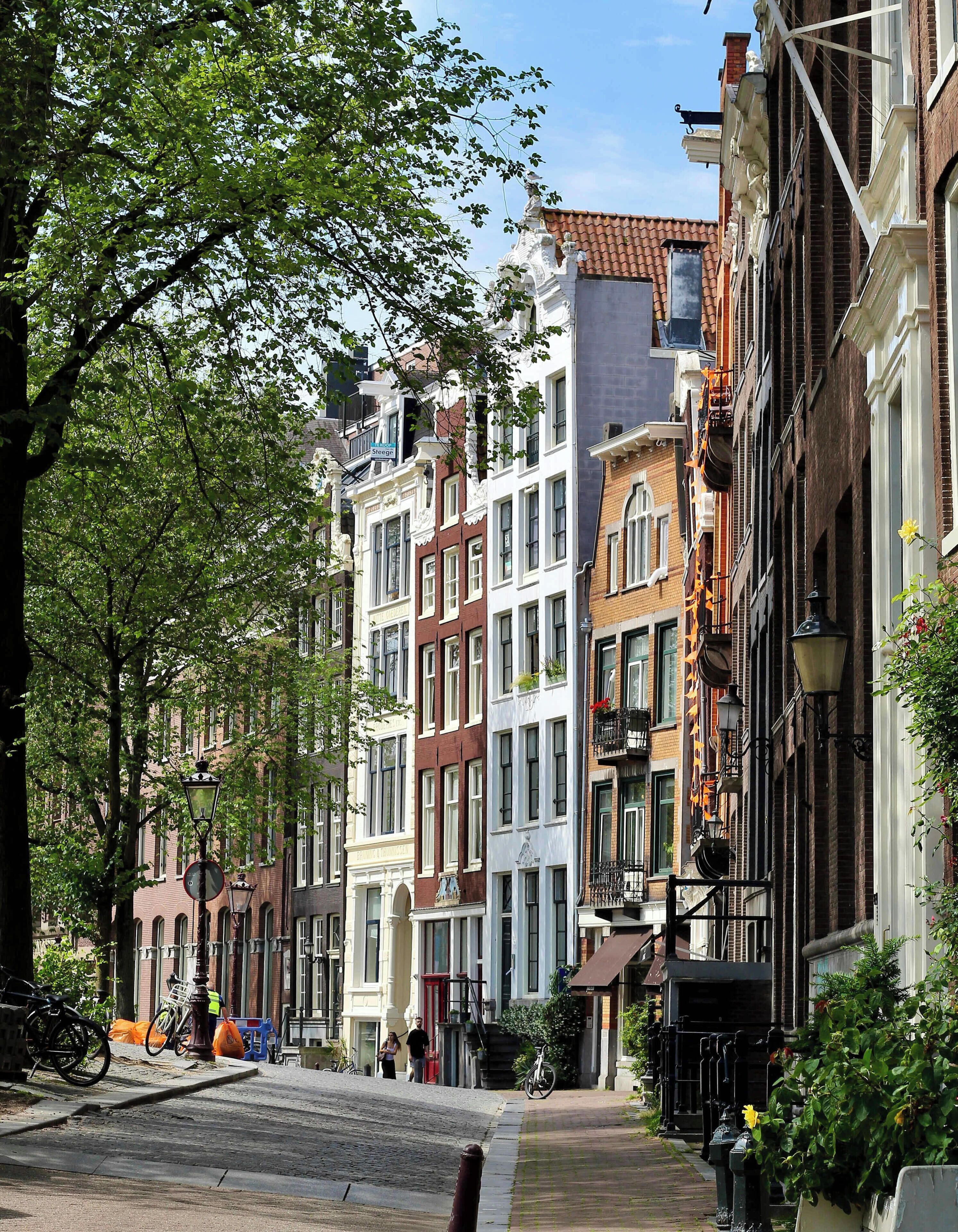 A row of multi-story buildings with a cobblestone street, a bicycle, and a pedestrian.